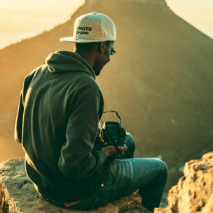 A man sitting on a step in the mountains with a camera in his hands.